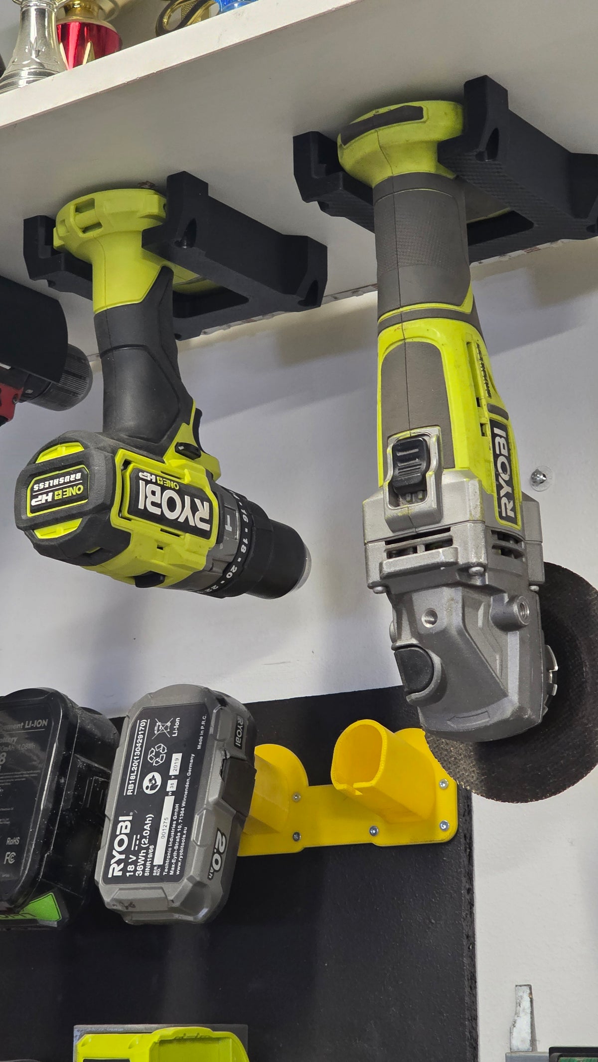 3D-tulostettu Ryobi One+ -koneteline hyllyn alle kiinnitettynä, koneet roikkuvat telineessä