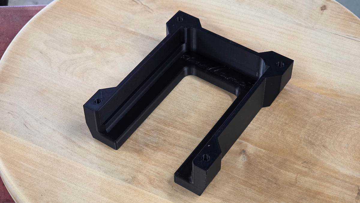 Musta 3D-tulostettu Ryobi One+ -yhteensopiva koneteline puisen levyn päällä